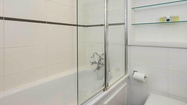 A bathroom with a glass-enclosed shower, a white toilet, and a shelf with toiletries. - At Home in Marylebone (London)