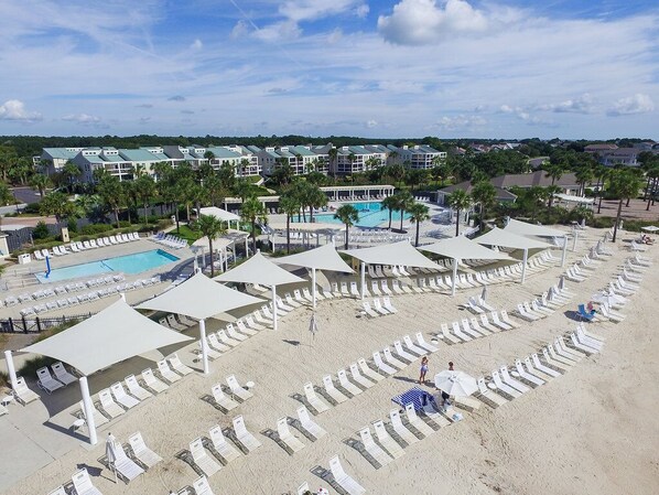 A resort with a pool, beach chairs, umbrellas, and a view of the surrounding area.