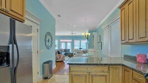 A kitchen with wooden cabinets, a stainless steel refrigerator, a water dispenser, and a dining area with a table and chairs. - Steps to Beach-Ocean views with both lake & pool (Panama City Beach)