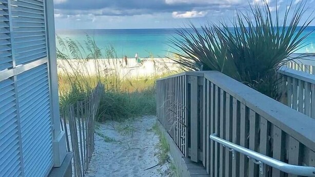 A wooden staircase leading to a beach with a clear view of the ocean and a cloudy sky. - Steps to Beach-Ocean views with both lake & pool (Panama City Beach)