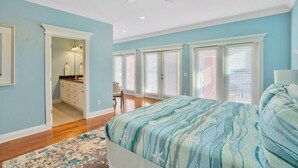 A bedroom with a large bed, a ceiling fan, and a view of the bathroom. - Steps to Beach-Ocean views with both lake & pool (Panama City Beach)