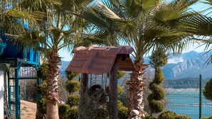 A courtyard with a decorative metal urn, palm trees, and a view of the sea. - Dolphin Boutique Hotel & Restaurant (Bucak)