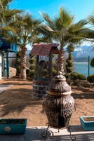 Een binnenplaats met een decoratieve metalen urn, palmbomen en uitzicht op zee.