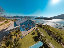 Un edificio azul con un cartel que dice "DOLPHIN BOUTIQUE HOTEL & RESTAURANT" con vista a un lago y montañas al fondo.