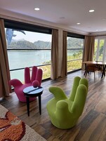 Una habitación moderna con ventanas amplias que ofrecen vista al lago, un comedor y sillas coloridas.