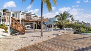 A beachfront property with a wooden deck, a covered outdoor area, and a two-story building with a balcony. - Marathon FL Waterfront Home | 30ft Dock (Marathon)