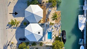 An aerial view of a beachside property with a swimming pool, two large umbrellas, and a dock with boats. - Marathon FL Waterfront Home | 30ft Dock (Marathon)