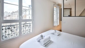 A hotel room with a bed, two windows, a balcony with metal railings, and a mirror on the wall.