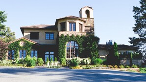 Uma casa grande com um campanário, janelas em arco e um jardim com diversas plantas e flores.