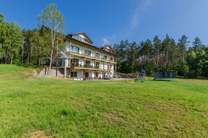 A multi-story building with a balcony, surrounded by a grassy field and trees. - Źródlo Raduni (gmina Stezyca)