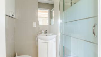 Een moderne badkamer met een toilet, een wastafel met spiegel erboven en een douchecabine met glazen wanden.