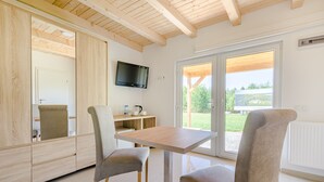 A modern room with a wooden ceiling, a TV mounted on the wall, a table with chairs, and a view through a large window. - Źródlo Raduni (gmina Stezyca)