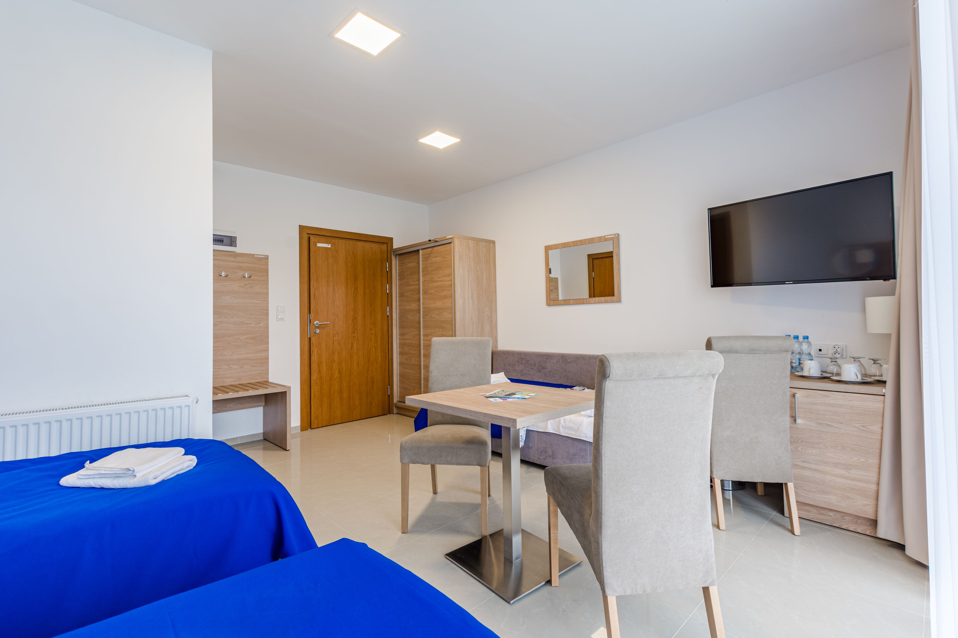 Habitación de hotel con dos camas, una mesa de comedor, sillas, televisor, espejo y kitchenette.