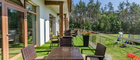 A patio with wicker furniture, a glass door entrance, and a playground in the background.