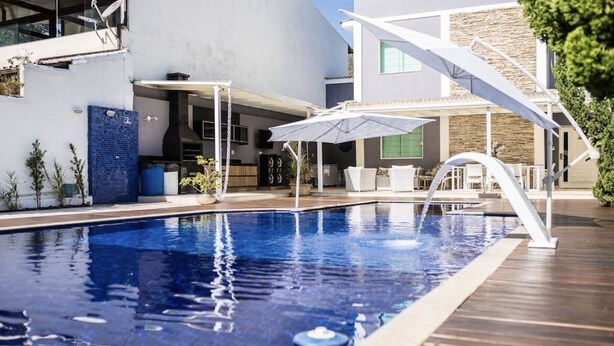 En swimmingpool med træterrasse, udendørs møbler og en overdækket patio.