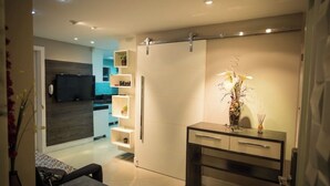 En moderne stue med et fladskærms-tv, en sofa, et skrivebord og indbyggede reoler med dekorative genstande.