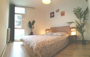 Une chambre à coucher avec un lit, une table de chevet, une plante en pot et une fenêtre.