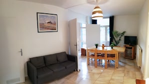 A living room with a dark grey sofa, a dining table with wooden chairs, a TV, and a potted plant. - Résidence du Parc des Tilleuls de LYON (4 bdrms, 82m²,free pkg, EUREXPO) (Lyon)
