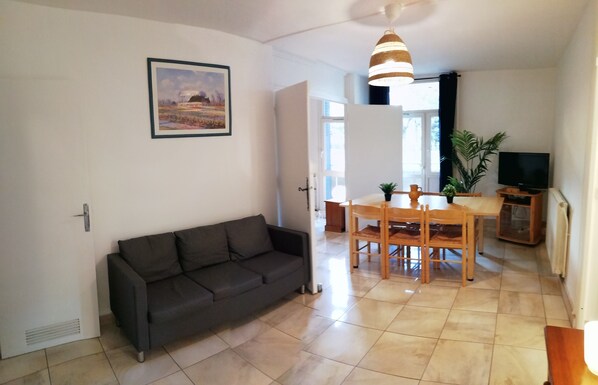 Un salon avec un canapé gris foncé, une table à manger avec des chaises en bois, un téléviseur et une plante en pot.