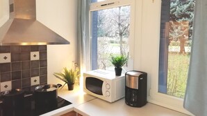 A kitchen with a stove, microwave, coffee maker, and a window with a view of trees. - Résidence du Parc des Tilleuls de LYON (4 bdrms, 82m²,free pkg, EUREXPO) (Lyon)