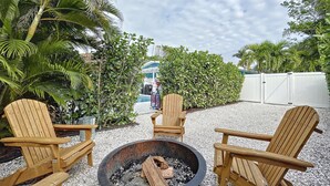 A fire pit area with wooden chairs and a pool in the background. - Charming Ground Level Resort Style 3 unit Condo  - unit C (Holmes Beach)