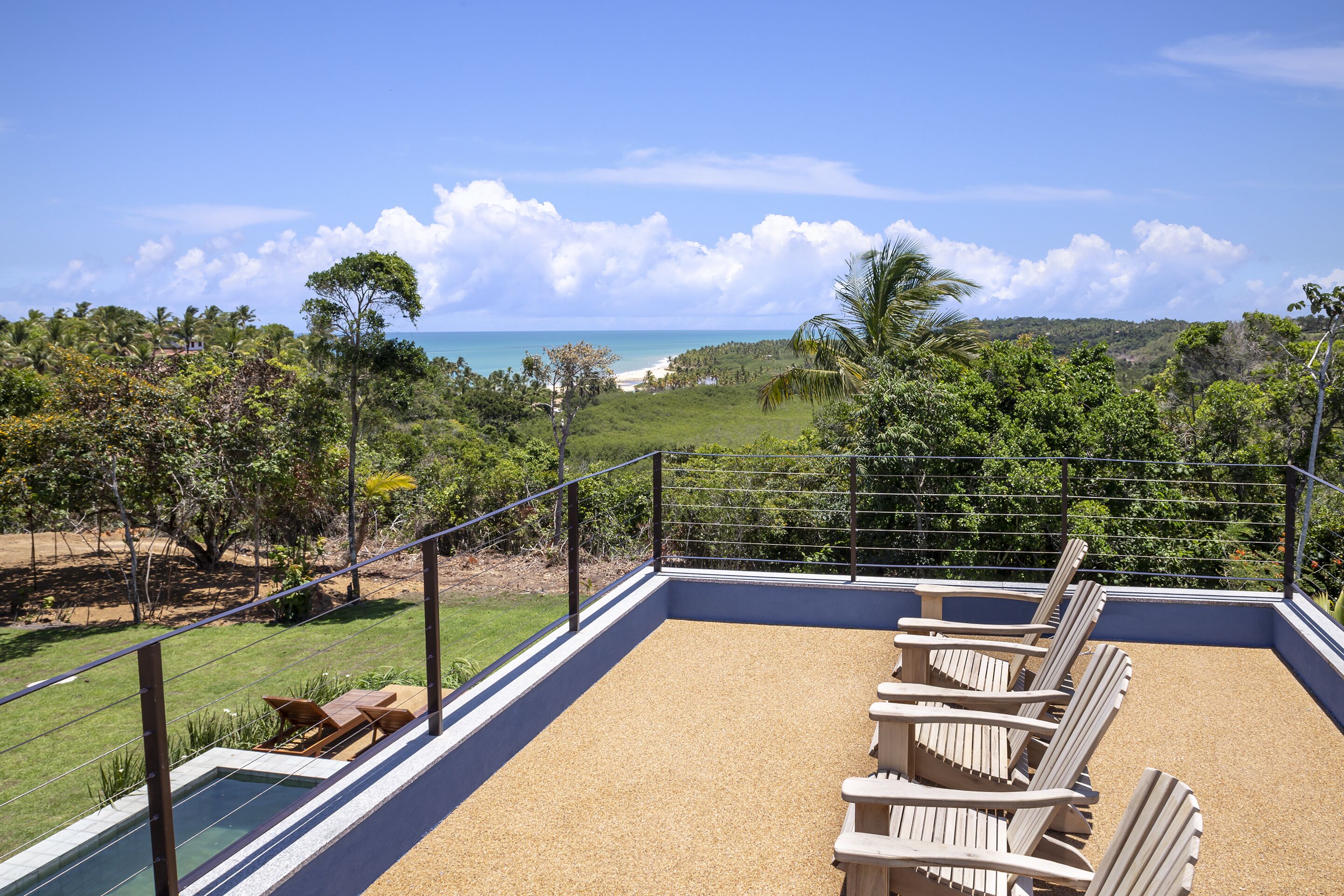 Eine Terrasse mit Pool, Liegestühlen und Blick auf Strand und Meer.