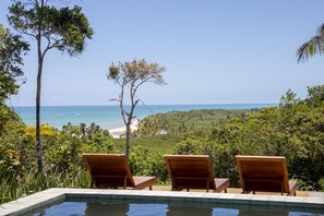 Un espace piscine avec des chaises longues donnant sur une plage et offrant une vue sur l’océan.