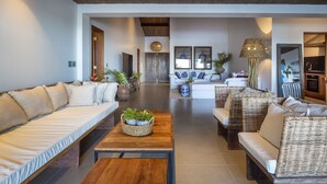 A spacious living area with a long sofa, a coffee table with a plant, and a wicker sofa. - Lux & Modern Villa w/ 5 bedrooms in Trancoso (BA)