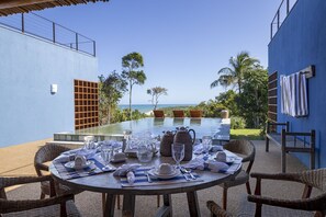 A dining table set for four with a view of the ocean and palm trees.