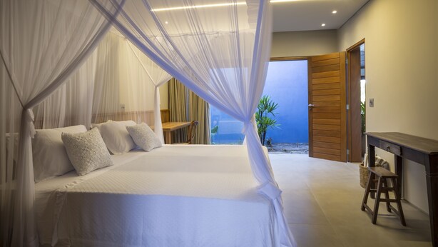 A bedroom with a bed, a nightstand, a wooden desk, and a view of the beach. - Lux & Modern Villa w/ 5 bedrooms in Trancoso (BA)