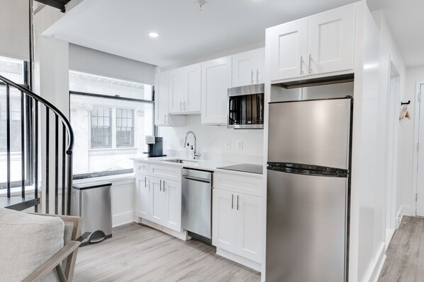 A modern kitchen with white cabinets, stainless steel appliances, a dishwasher, and a window providing natural light.