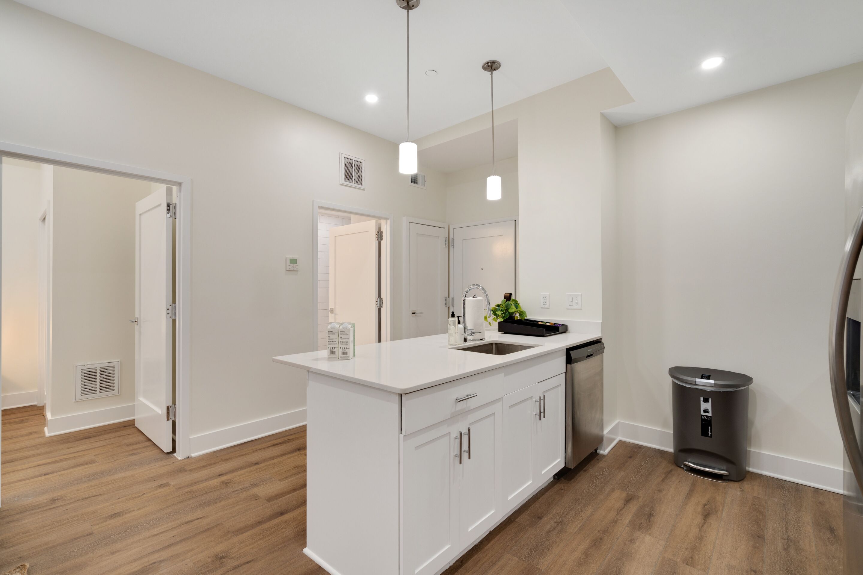 Una cocina moderna con armarios blancos, una isla central, electrodomésticos de acero inoxidable e iluminación colgante.