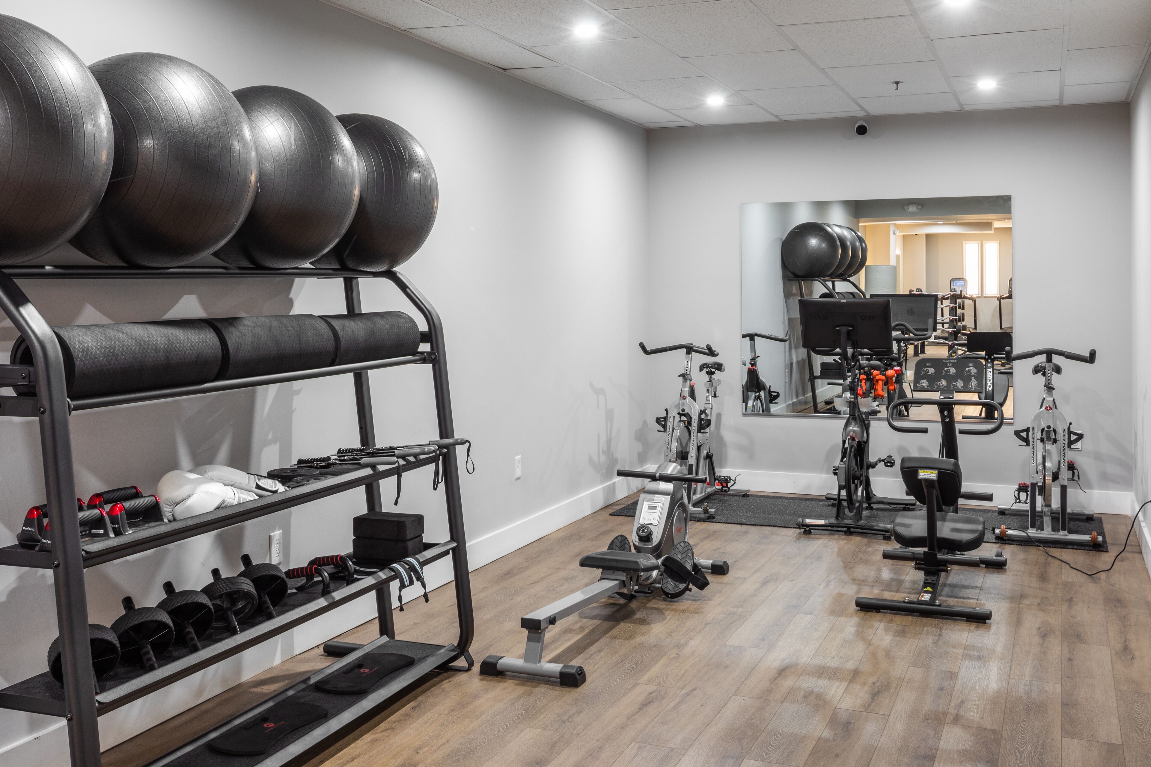 A gym with exercise equipment, a mirror, and a wooden floor.