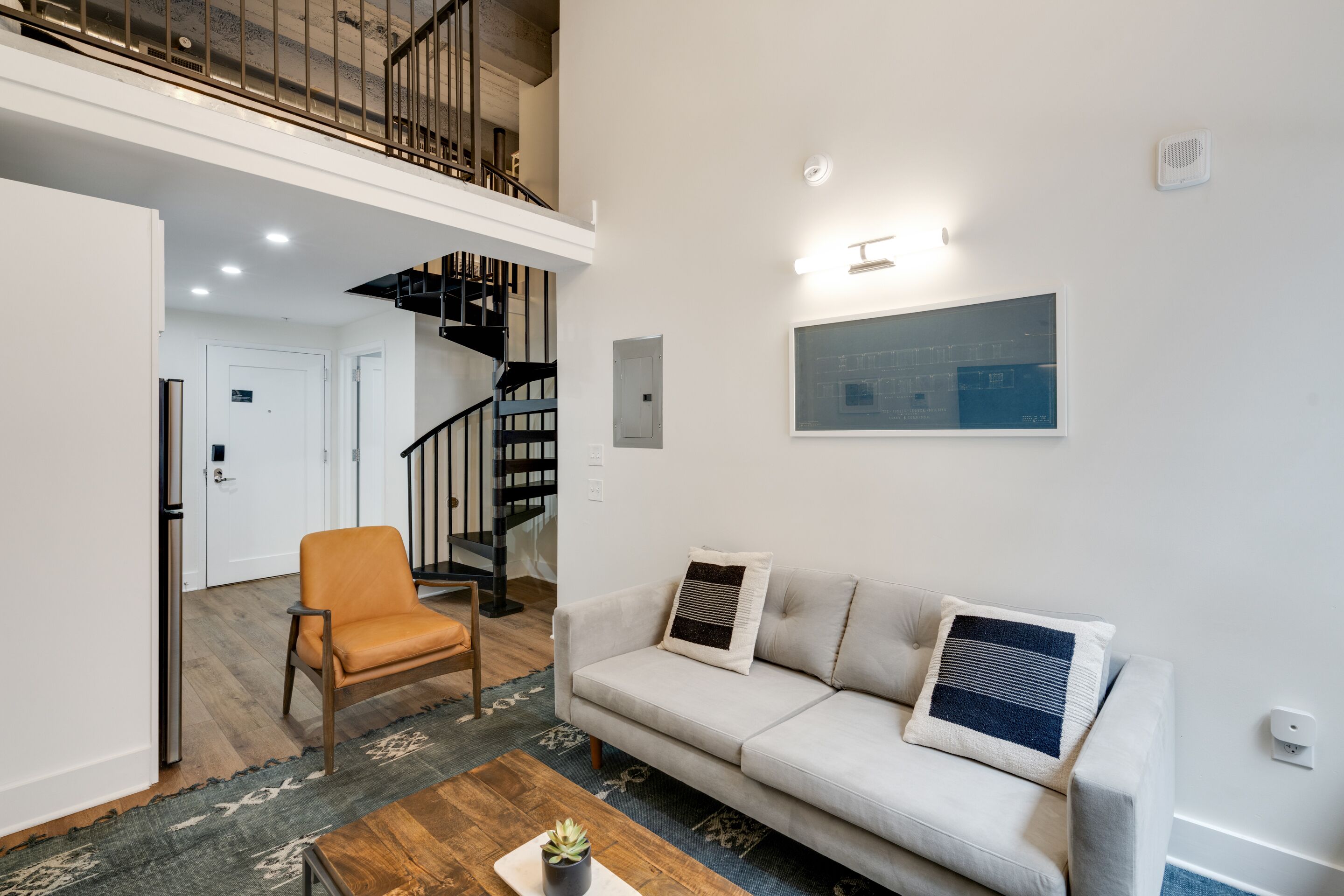 A modern living room with a sofa, armchair, and coffee table. A staircase leads to an upper level.