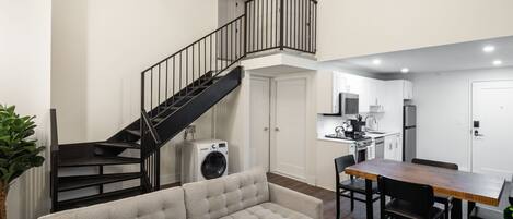 A modern apartment with a living room, dining area, kitchen, and a staircase to an upper level.