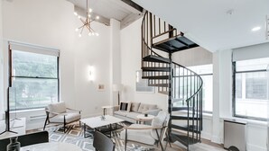 Una sala de estar moderna con una escalera en espiral, un conjunto de sofás, una mesa de comedor y ventanas amplias.