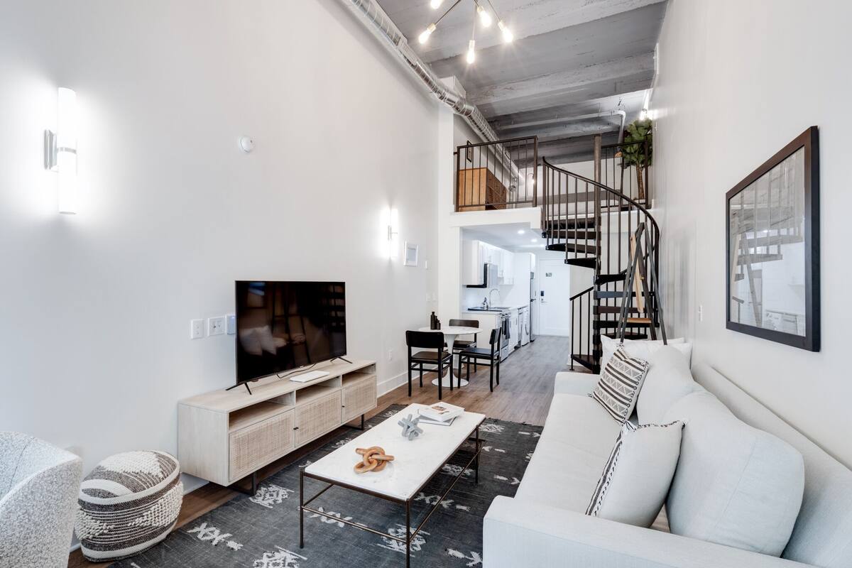 Ein modernes Wohnzimmer mit Flachbildfernseher, einer Couch, einem Couchtisch und einer Treppe, die zu einer oberen Ebene führt.