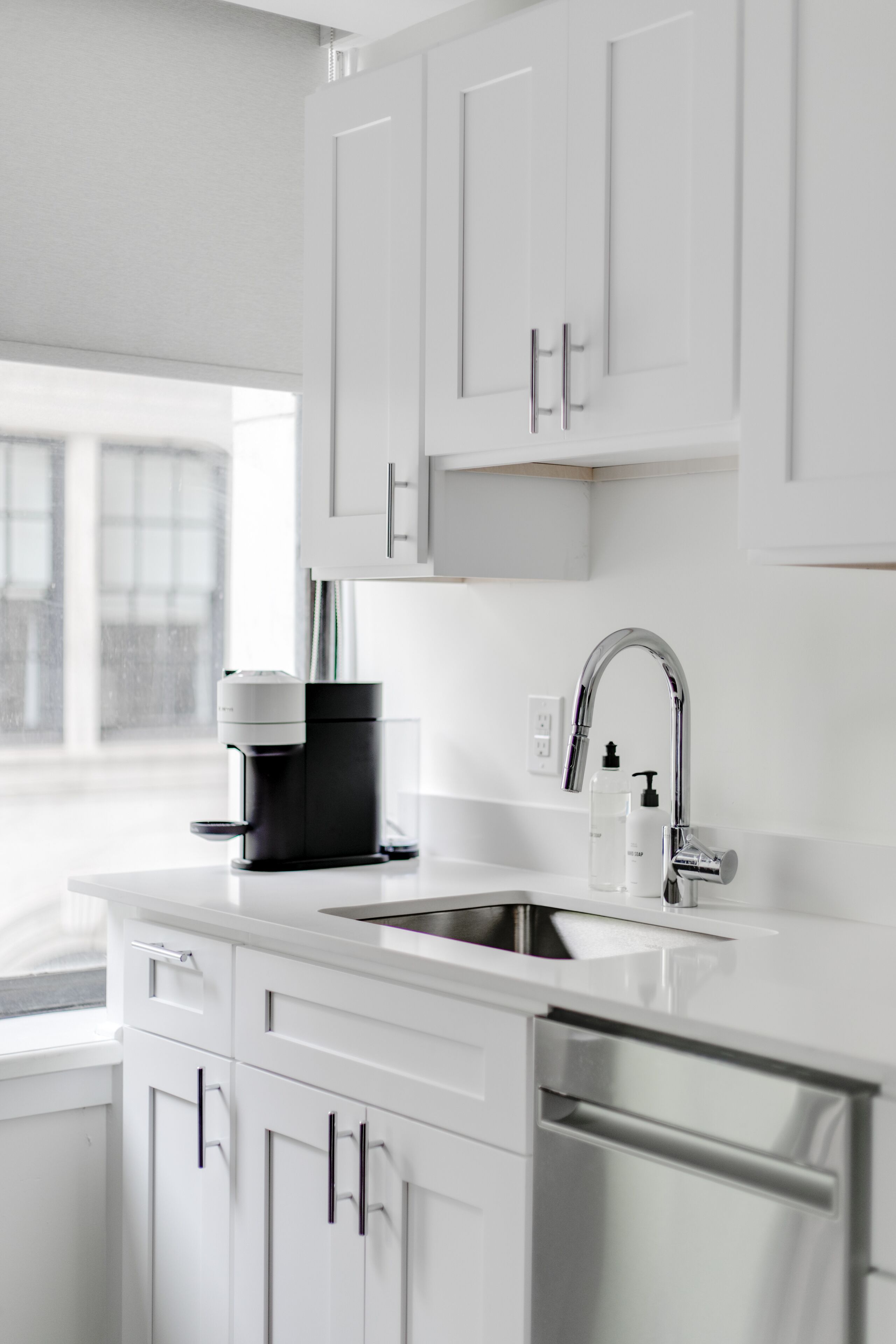 Een moderne keuken met witte kastjes, roestvrijstalen apparatuur en een raam dat voor natuurlijk licht zorgt.