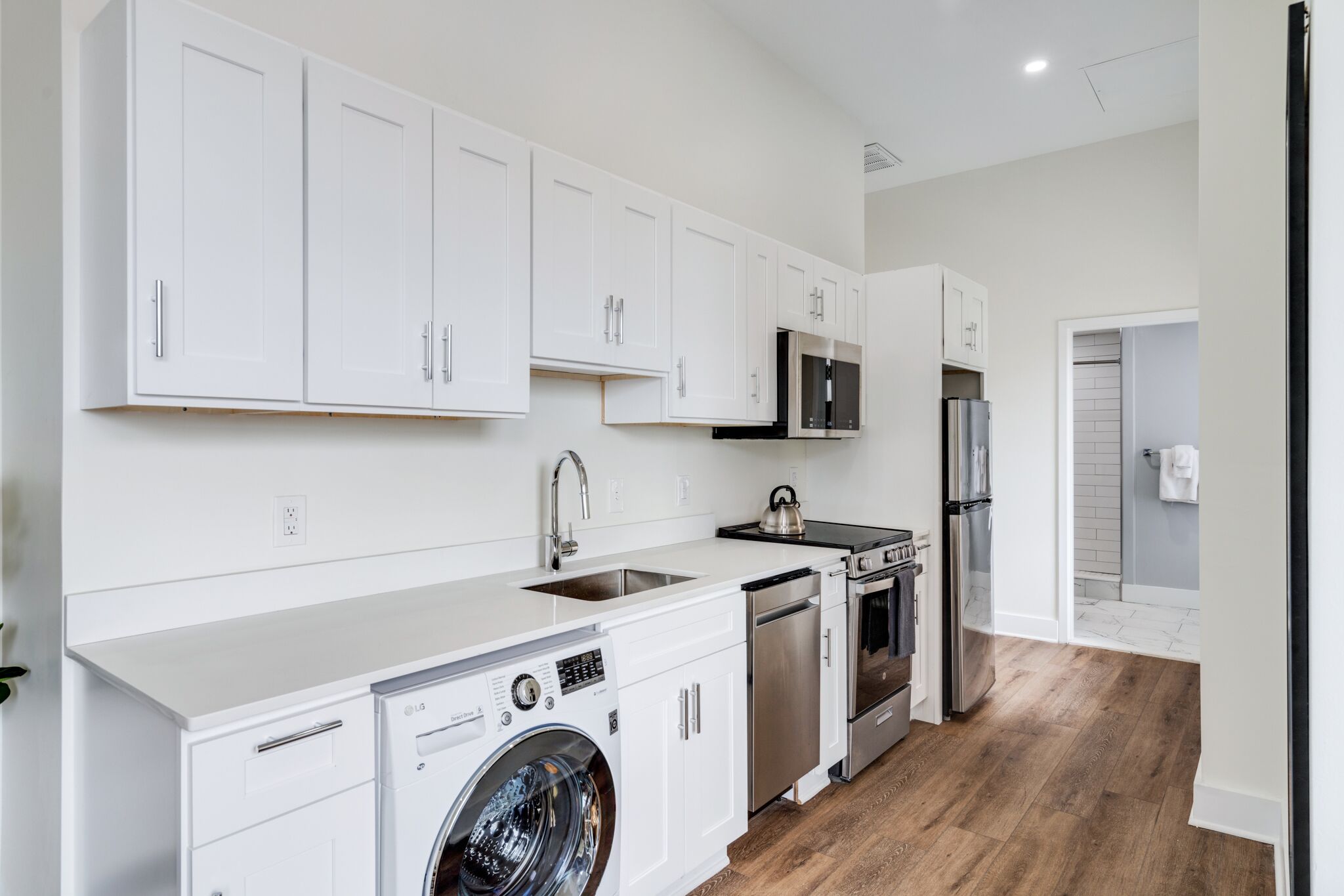A modern kitchen with white cabinets, stainless steel appliances, and a built-in washer and dryer.