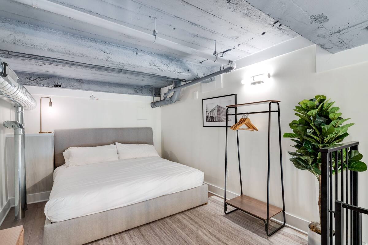 Ein modernes Schlafzimmer mit einem Bett, einem Heizkörper, einer Pflanze und einem Kleiderhaken.