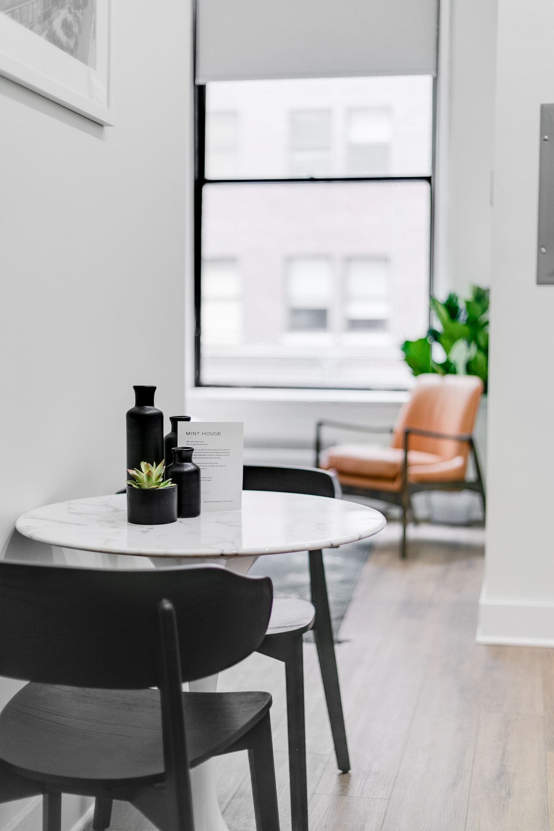 Um interior moderno com uma mesa redonda, cadeiras pretas, uma planta em vaso e um quadro na parede.
