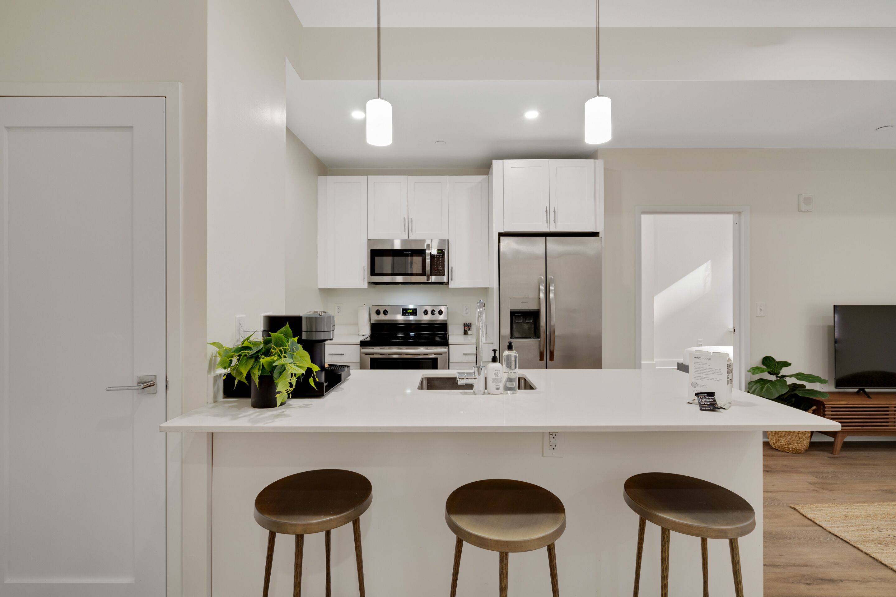Una cocina moderna con armarios blancos, electrodomésticos de acero inoxidable, una isla central con taburetes e iluminación colgante.