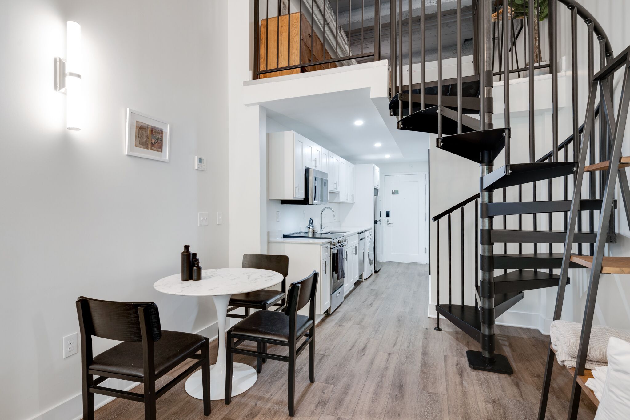 A modern kitchen with white cabinets, a black staircase, and a dining area with a round table and chairs.