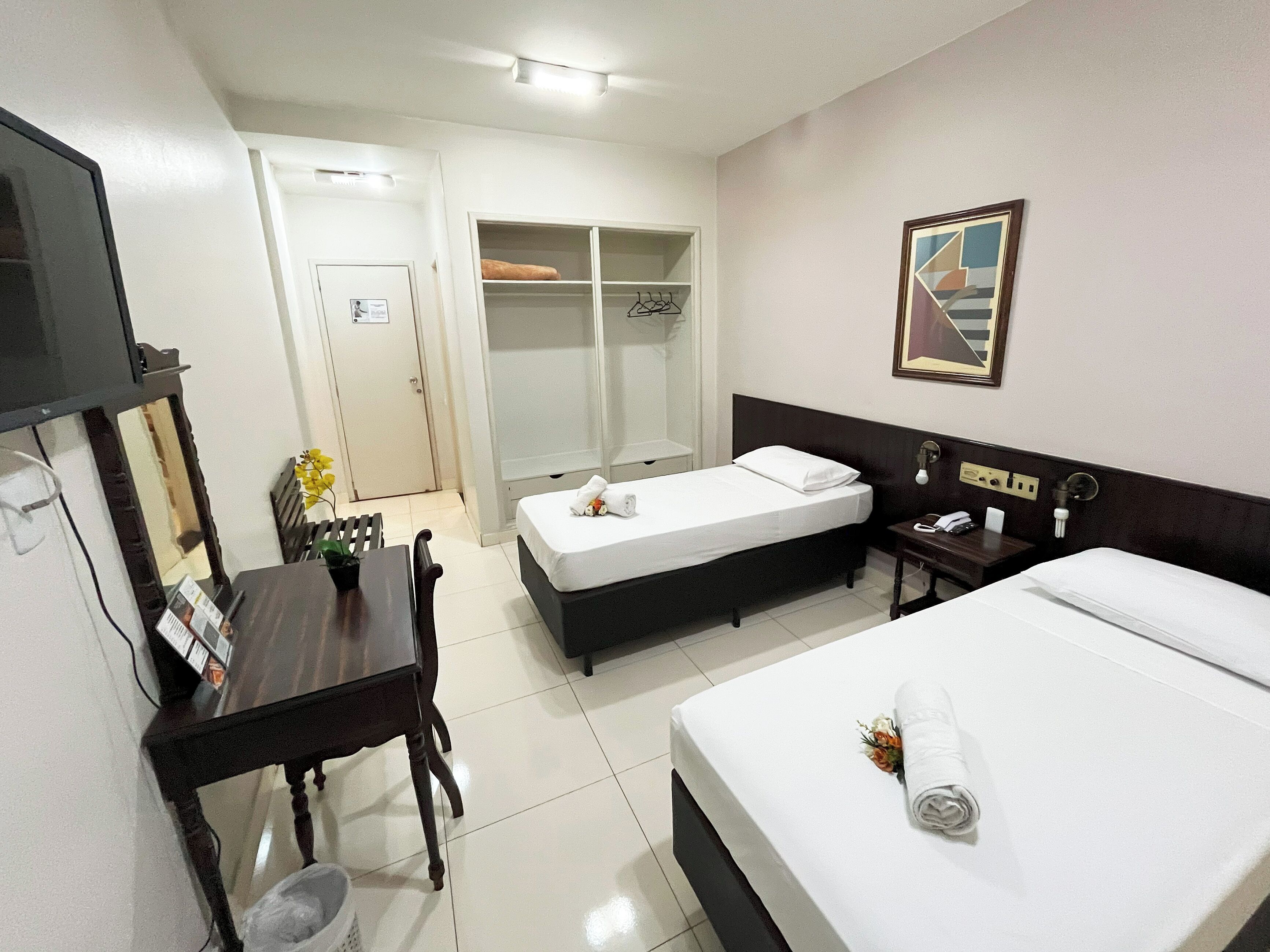 A hotel room with a bed, a desk with a chair, a wardrobe, and a television.