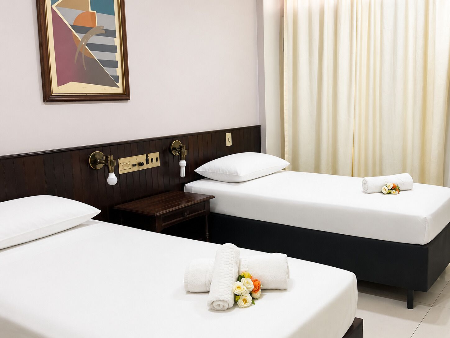 A hotel room with two beds, a nightstand, a wall-mounted lamp, and a painting.