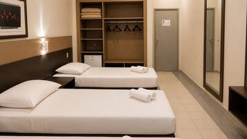 Quarto de hotel com duas camas, um guarda-roupa, um espelho e um pequeno frigorífico.
