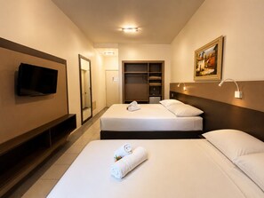Habitación de hotel con dos camas, un televisor, un armario, un cuadro y una lámpara de noche.