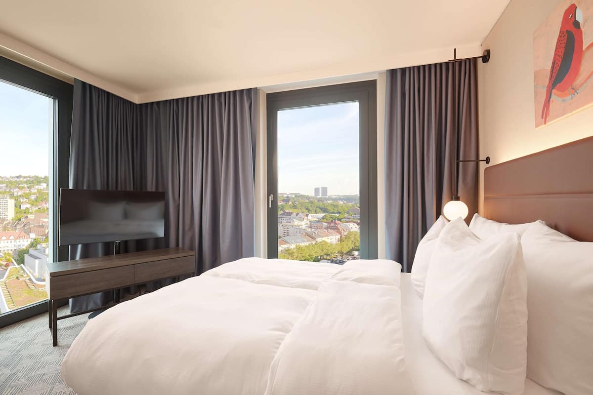 Une chambre d’hôtel avec un grand lit, un téléviseur à écran plat, une vue sur la ville et un tableau au mur.