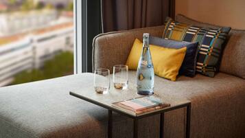 A modern hotel room with a sofa, a small table, a bottle, and two glasses.