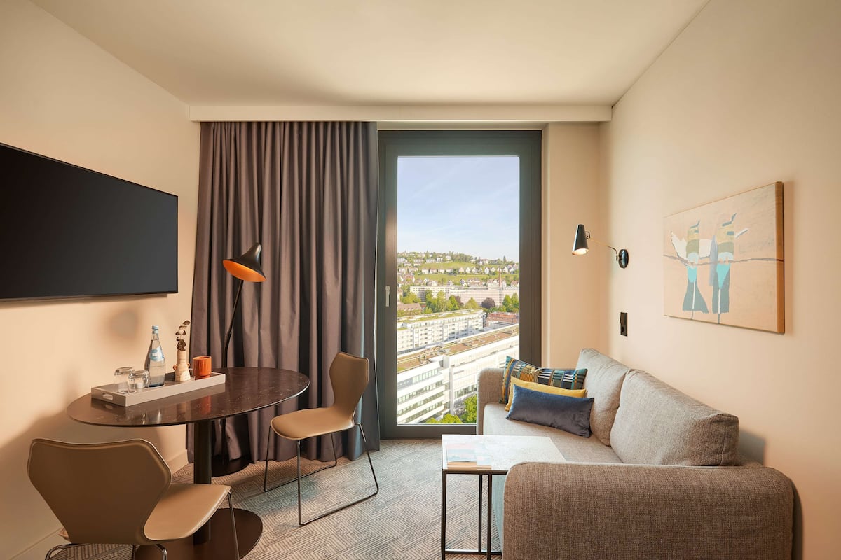 Une chambre d’hôtel avec une grande fenêtre, un canapé, une table à manger et un téléviseur.